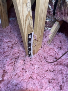 High-quality blown-in insulation in a new construction attic with a paper depth gauge showing R-49 to R-60 levels.